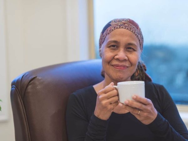 Senior ethnic woman with cancer sits by her window drinking tea